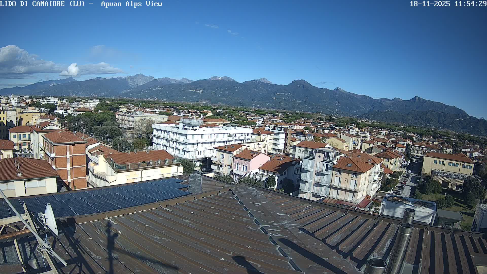 A high-angle view reveals a densely built town with varied architecture and solar panels, extending towards distant, hazy mountains under a heavily overcast sky.