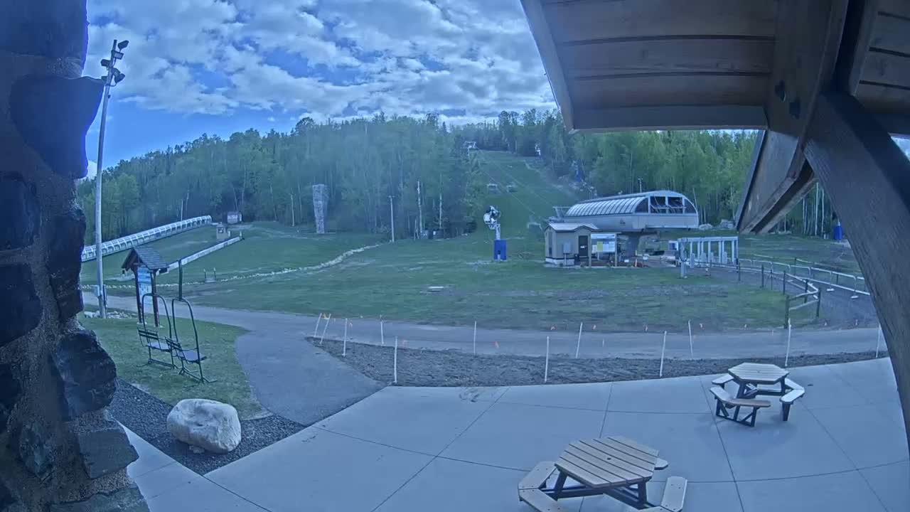 A ski hill with a chairlift and grassy areas is visible from a patio under an overcast sky.