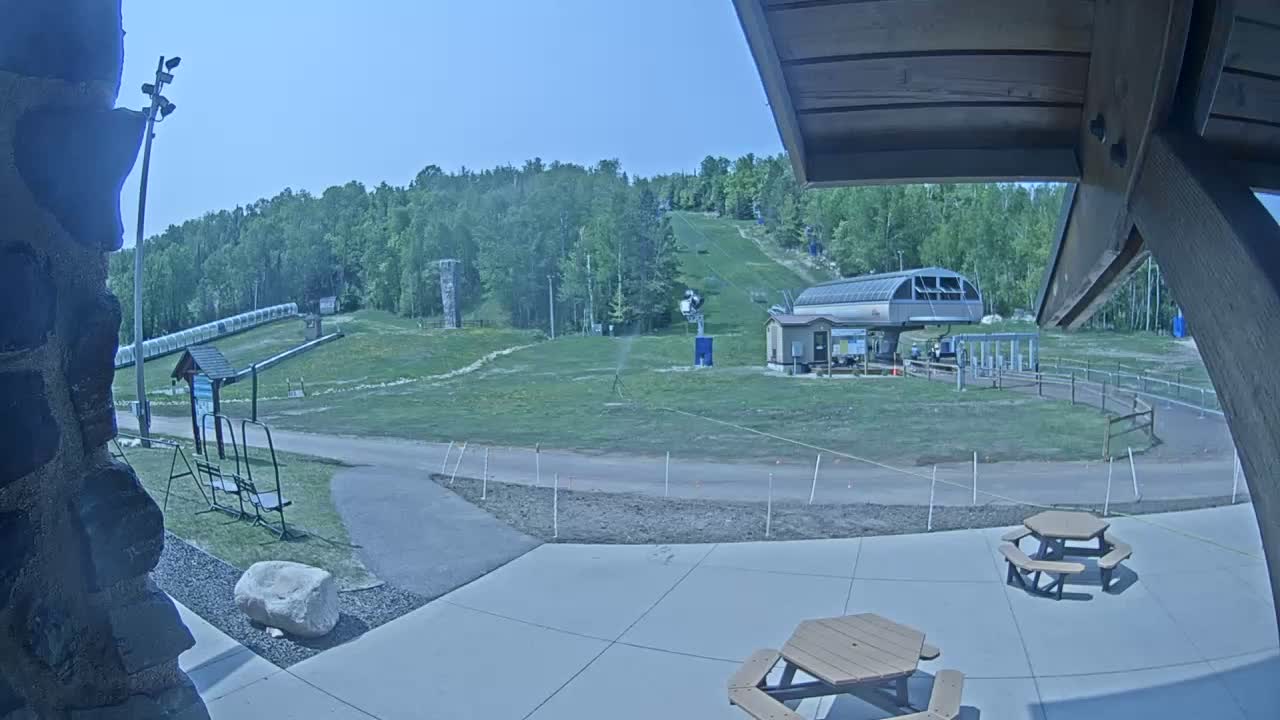 A grassy ski hill with a chairlift and a few picnic tables is visible on a sunny day.