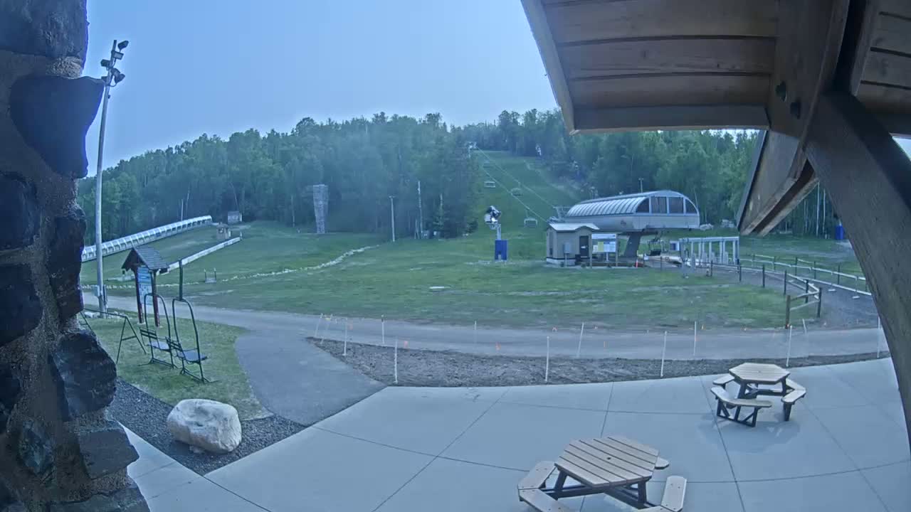 An outdoor view of a ski lift and grassy area on a clear evening, with two picnic tables in the foreground.