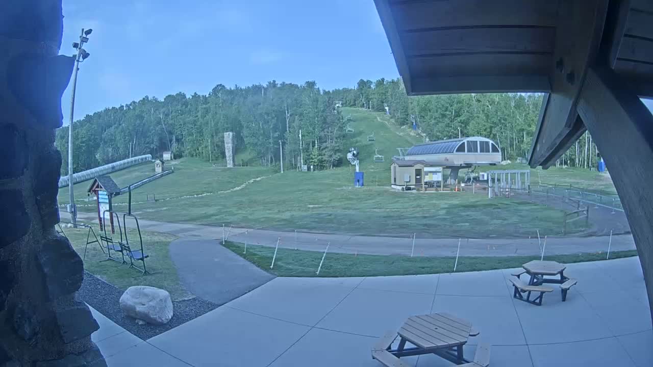 A grassy ski hill with a chairlift and picnic tables is visible under a clear sky.