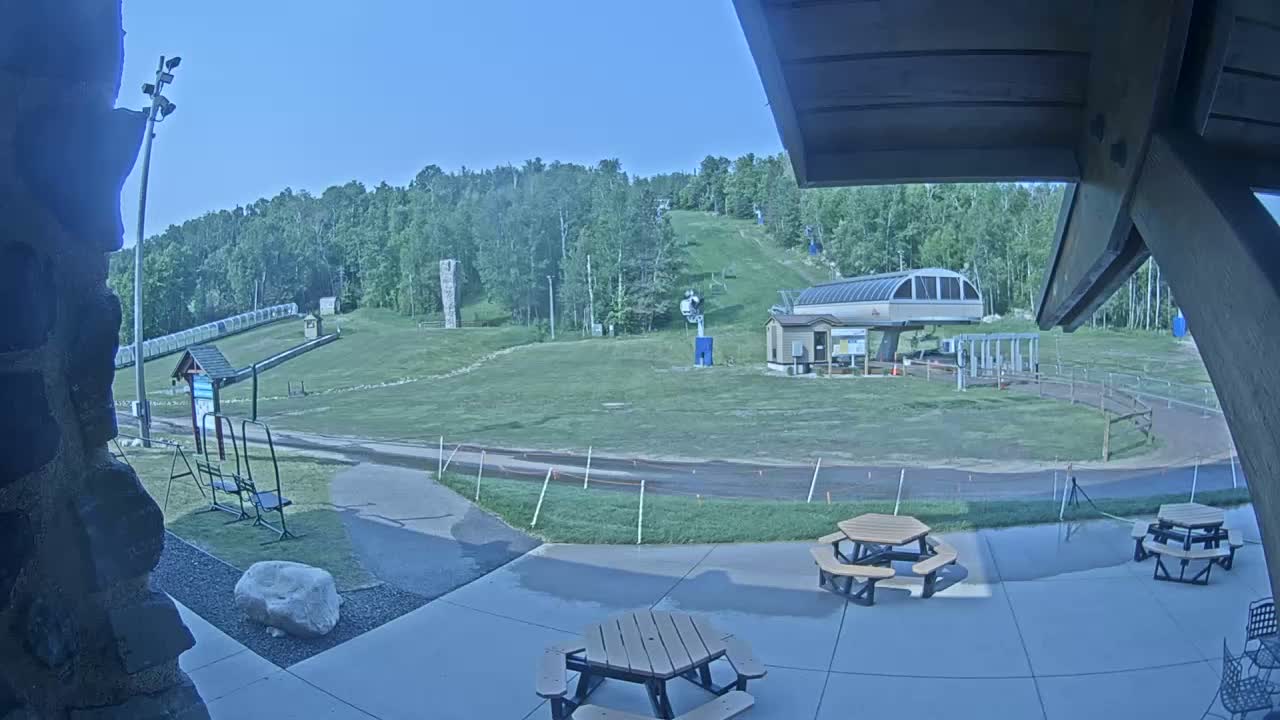 A grassy ski slope with a chairlift and picnic tables is visible on a clear, sunny day.