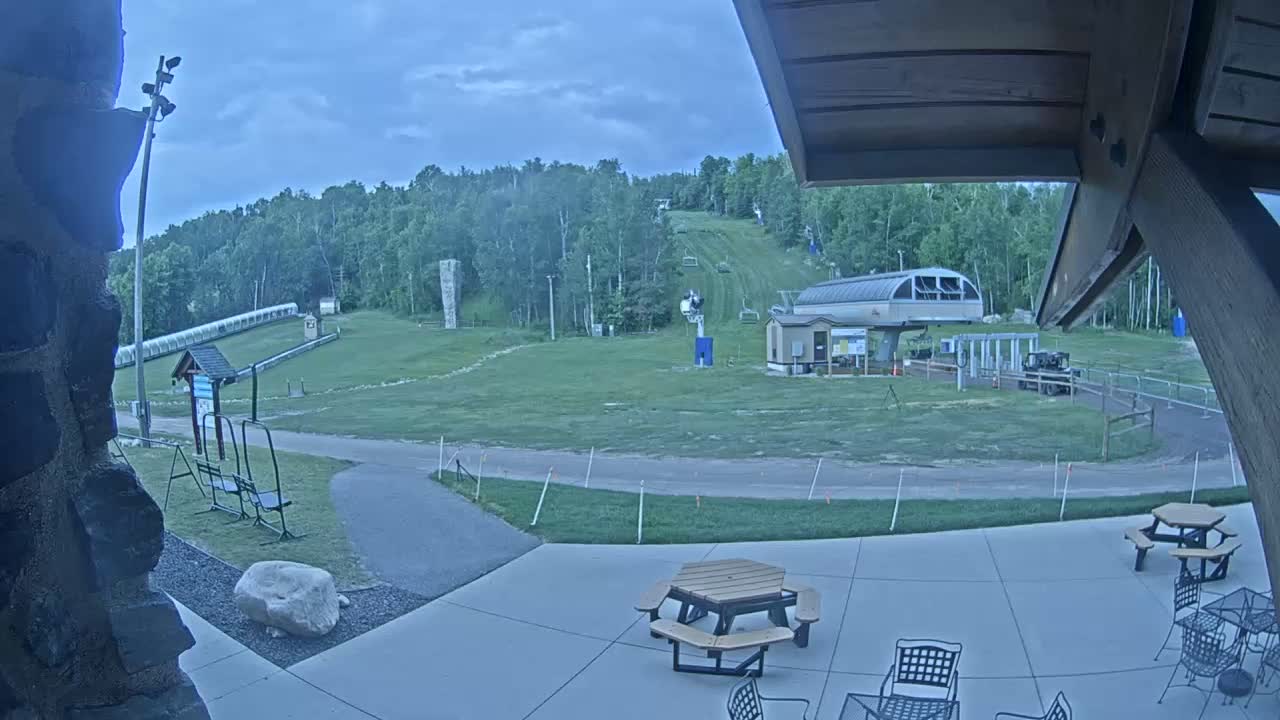 A grassy ski slope with a chairlift and picnic tables on a patio under an overcast sky.