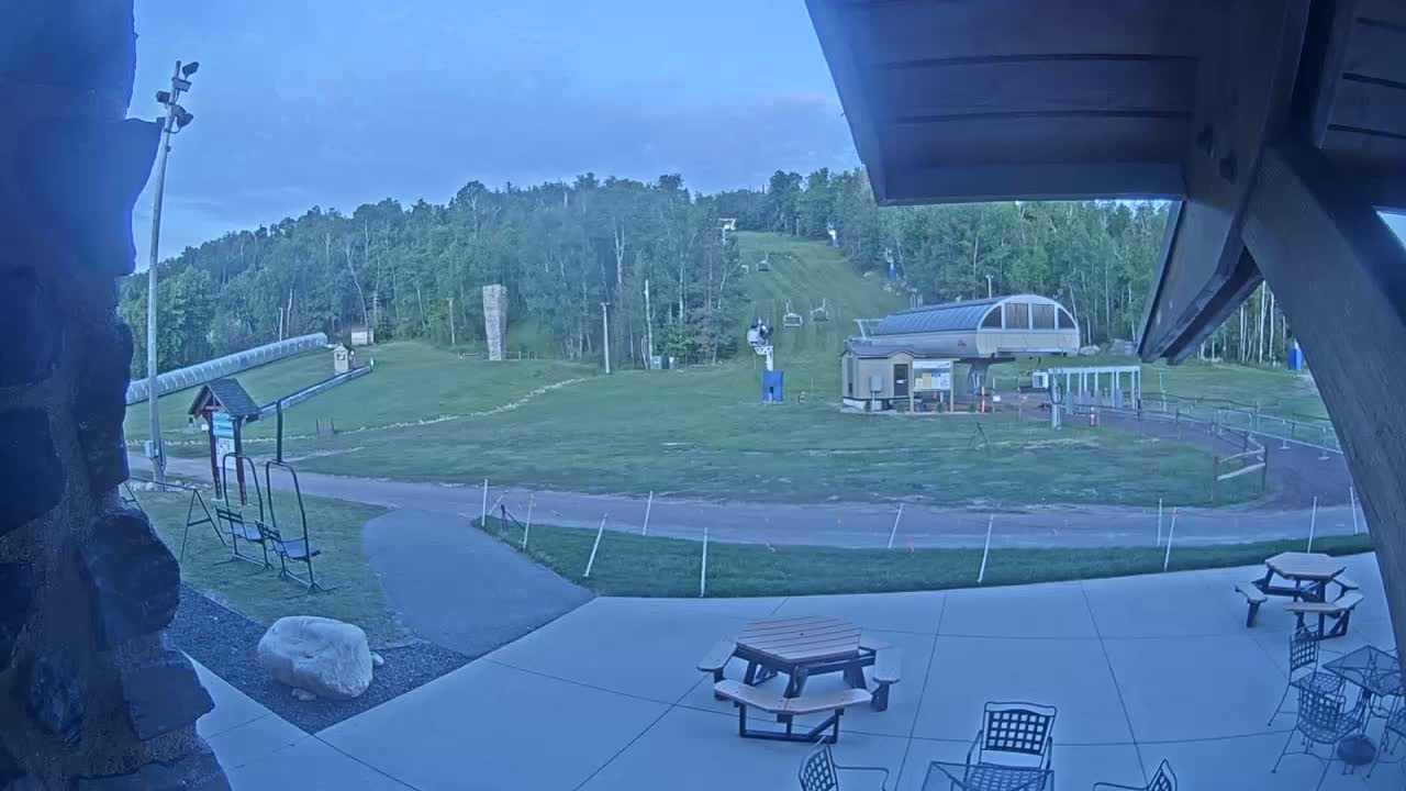 A grassy outdoor area with a ski lift, a covered patio with picnic tables, and a mostly clear evening sky.