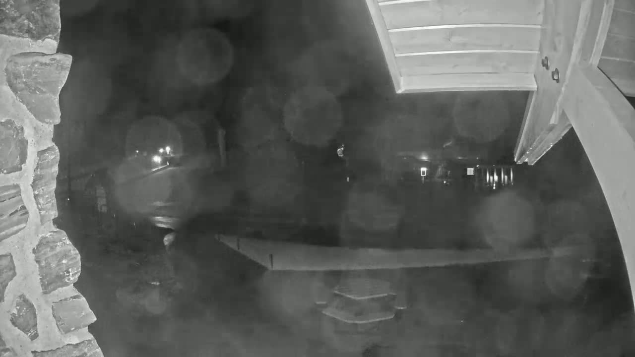 A nighttime, rainy scene shows a blurry figure near a stone wall, with headlights visible in the distance.