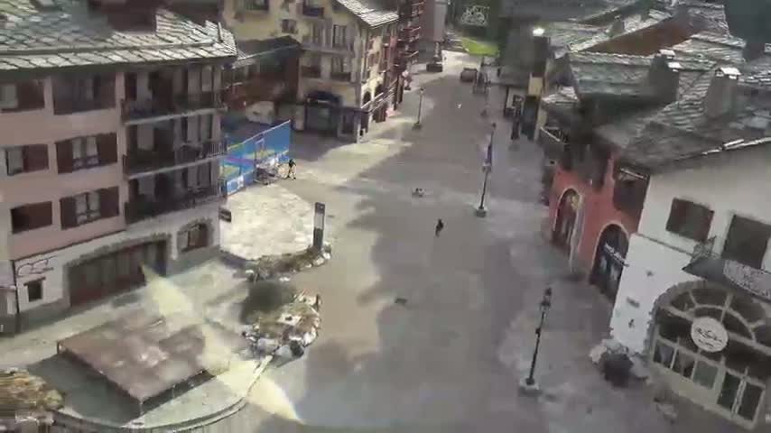 A mostly empty village square with several multi-story buildings, partially flooded, under a cloudy sky.
