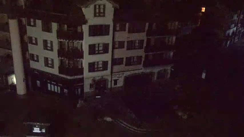 A nighttime aerial view shows a dark, multi-story building with numerous windows, situated in a dimly lit area.
