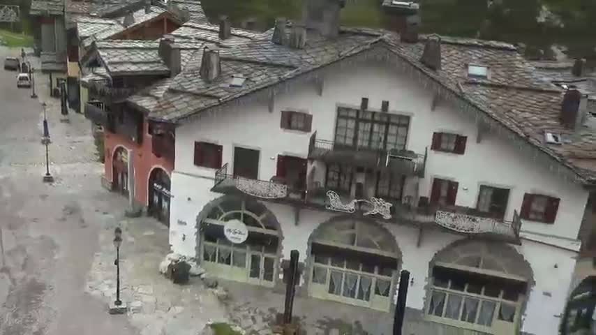 A village of stone buildings with icicles hanging from the roofs sits under a gray sky on a wet, possibly snowy, day.