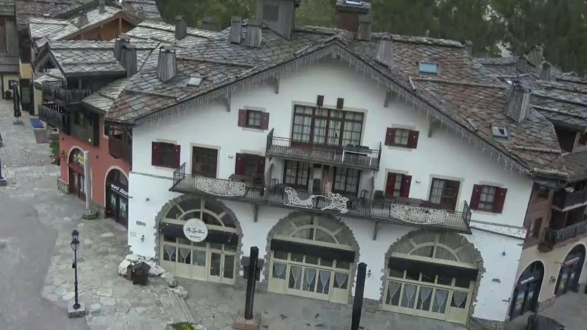 An overhead view of a European-style village with a large, white building featuring arched doorways and multiple balconies, under an overcast sky.