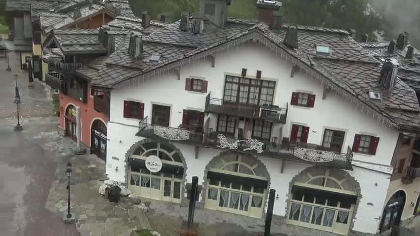 A cluster of European-style buildings with slate roofs and icicles hangs from the eaves, situated in a wet, possibly snowy, environment.