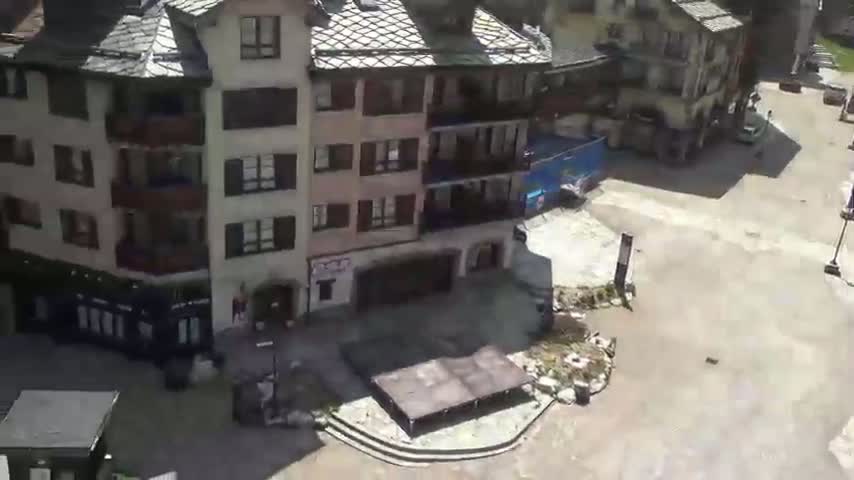A paved plaza with several multi-story buildings surrounds it, under a bright, sunny sky.