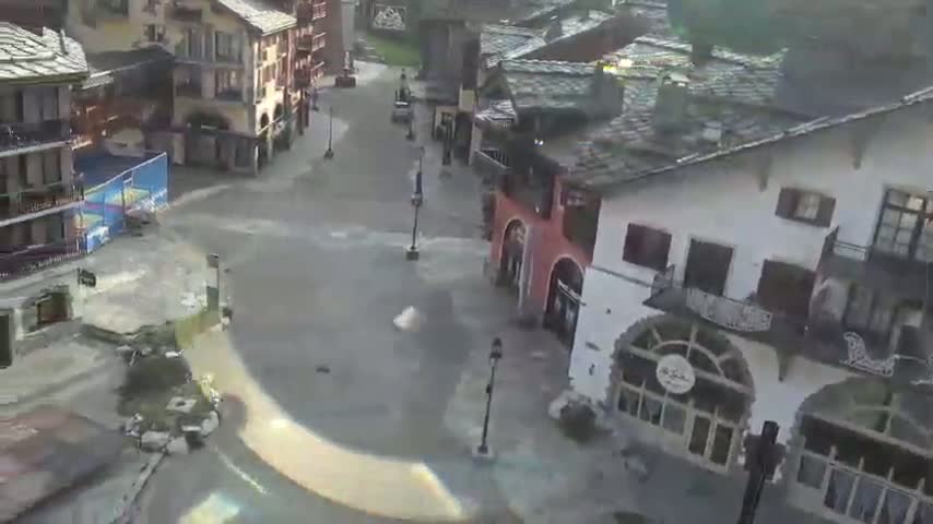 Floodwaters cover a paved street and plaza in a village of European-style buildings.