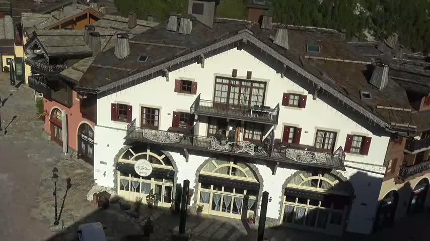 A large, white building with multiple balconies and arched windows, surrounded by other smaller buildings on a sunny day.