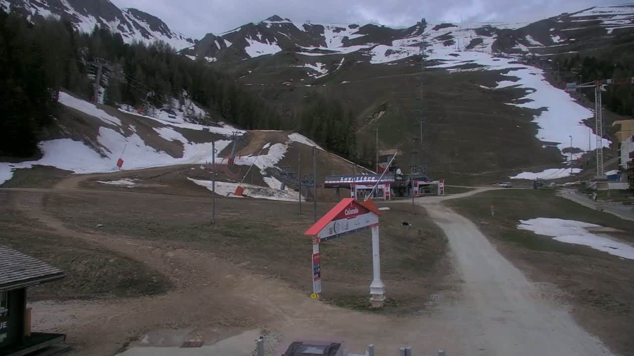 A mostly barren ski slope with patches of snow under a cloudy sky.