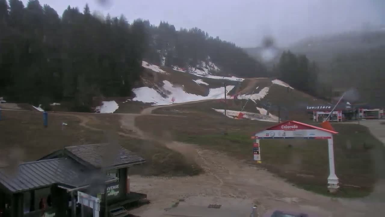 A rain-soaked ski resort with patches of remaining snow on the slopes, a few buildings, and a mostly brown landscape.