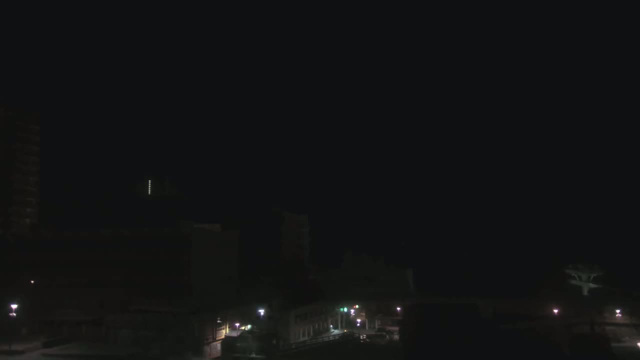 A nighttime view of city buildings and streets, dimly lit by streetlights under a dark sky.
