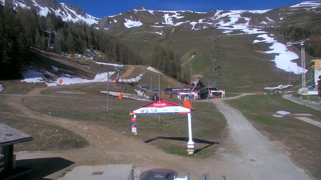 A ski resort in the mountains on a sunny day with patches of snow remaining on the slopes and surrounding hills.