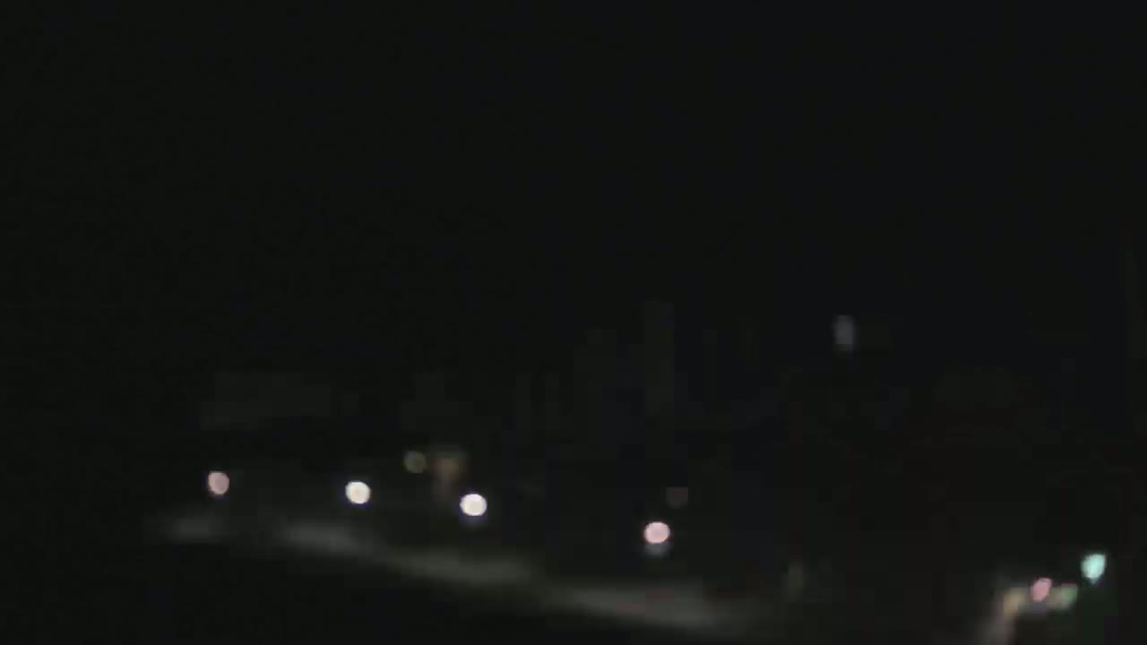 A blurry nighttime image shows a distant city skyline with a few faint lights visible in the foreground.