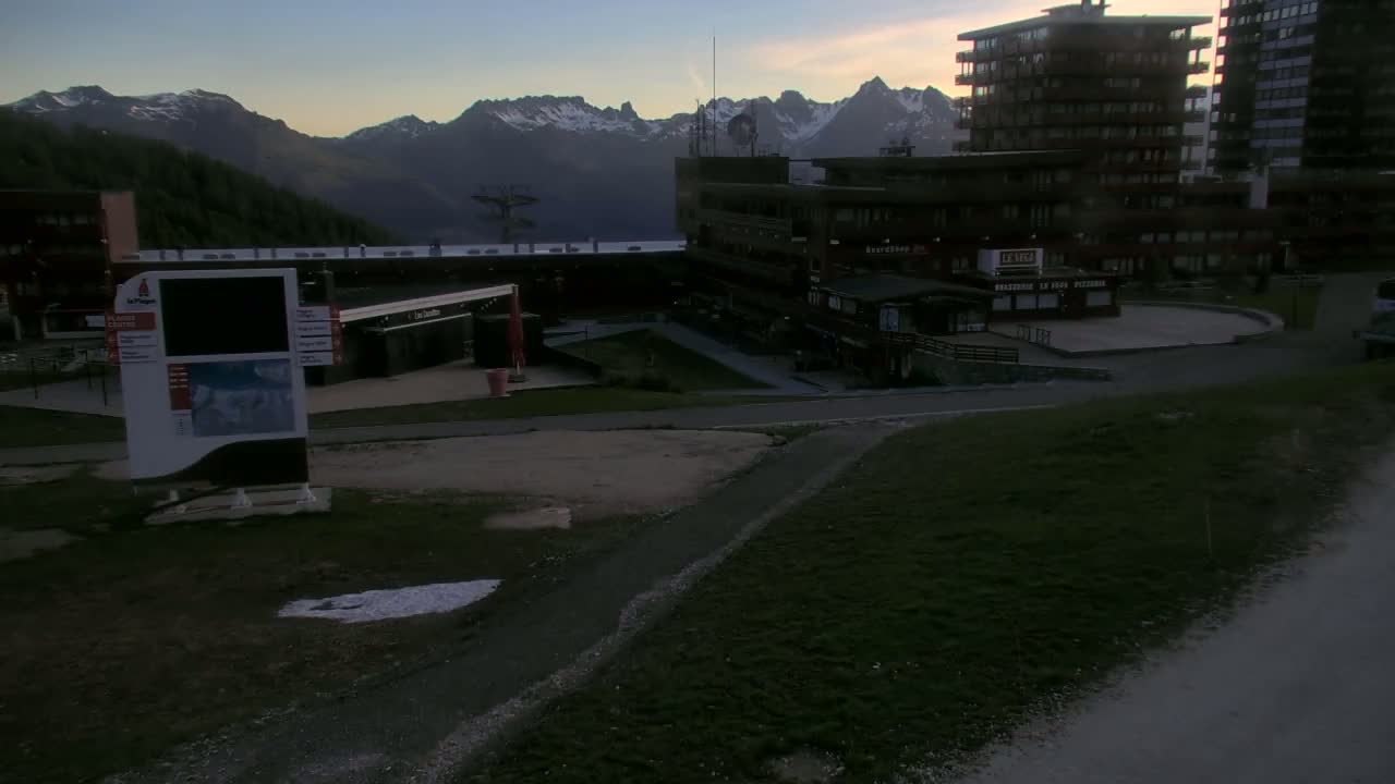 A mountain vista is visible behind a plaza with several buildings at dusk, under a clear sky.