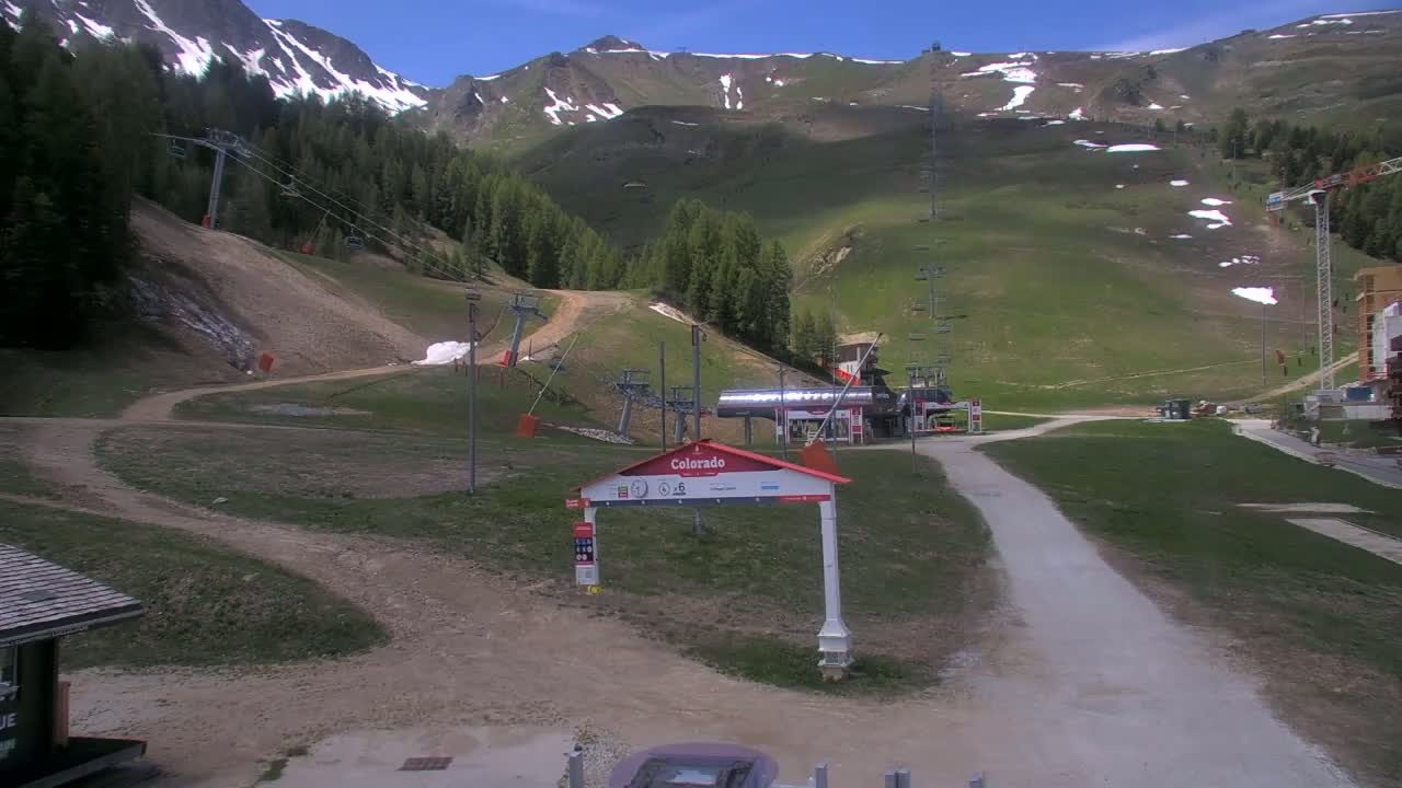 A ski resort in the mountains on a sunny day with patches of snow remaining on the higher slopes.