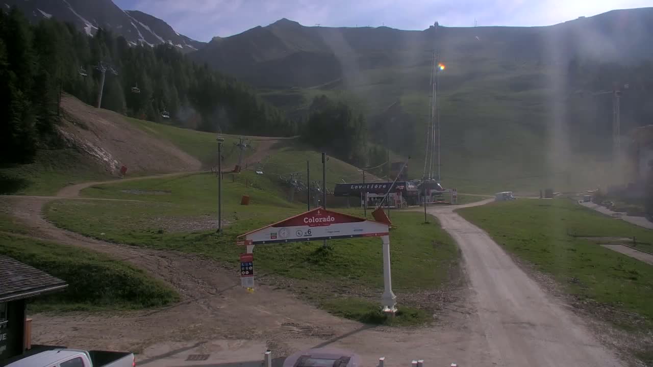 A grassy mountainside ski resort with chairlifts, a dirt road, and a hazy, sunny day.