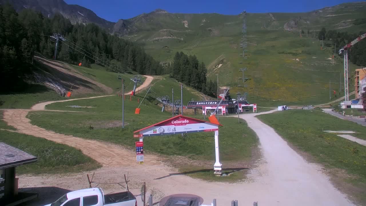 A mountainside ski resort with chairlifts and dirt roads, under sunny skies.