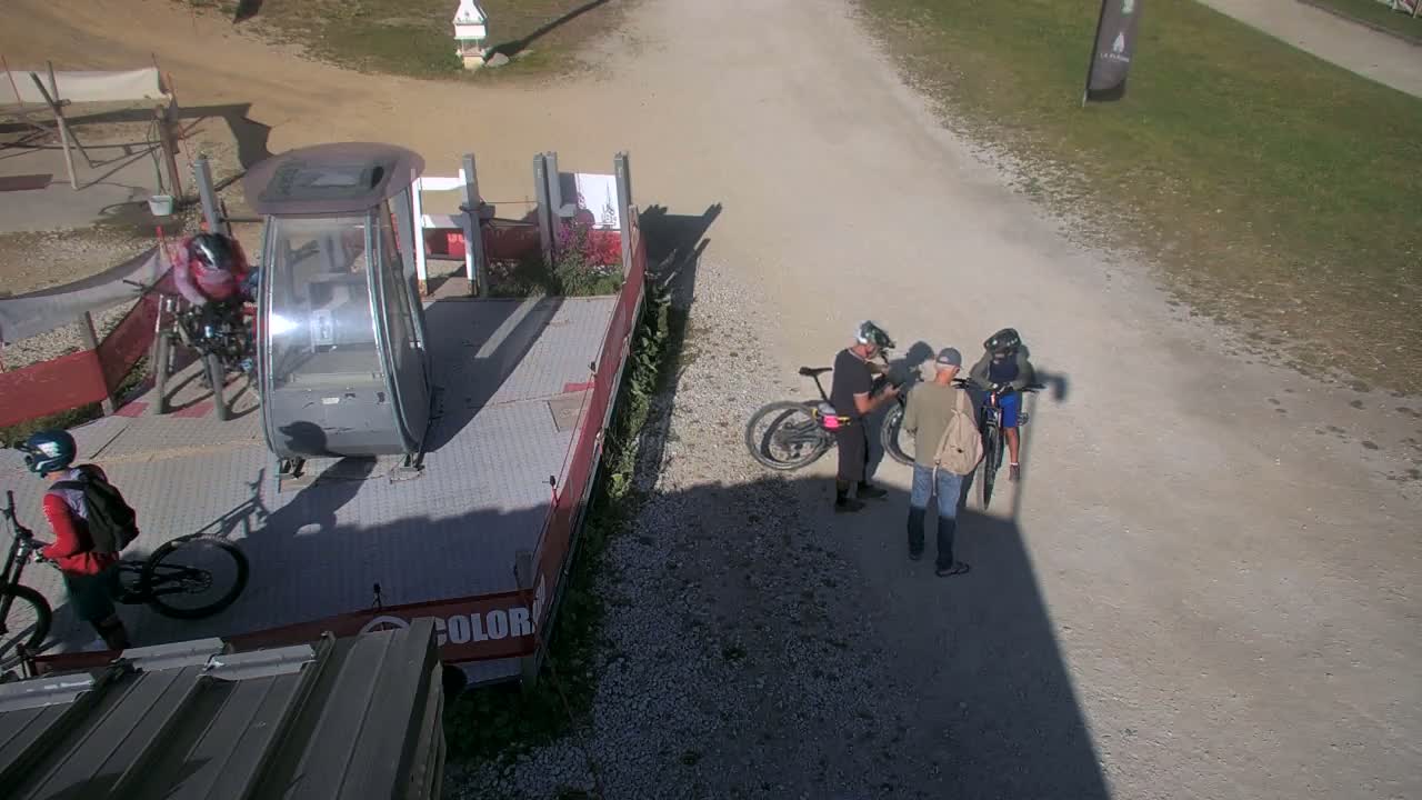 Several people with mountain bikes stand near a chairlift on a sunny day.
