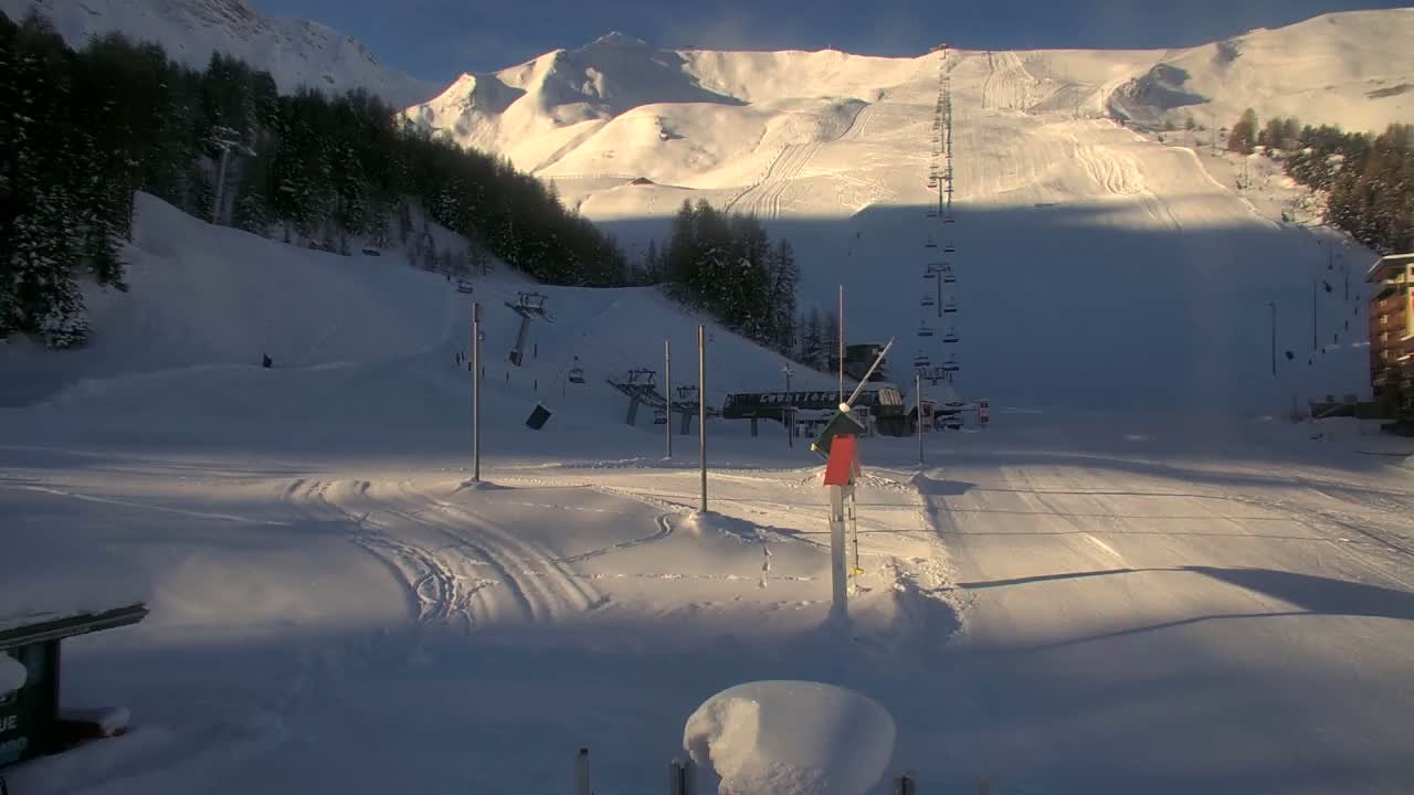 A snow-covered ski resort with multiple ski lifts, forested slopes, and distant mountains is visible under clear, sunny skies.