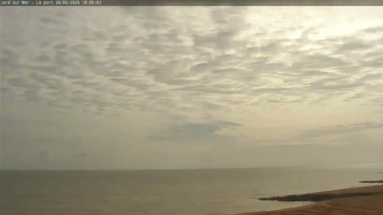 A calm sea under a mostly cloudy, light-grey sky is shown from a high vantage point.