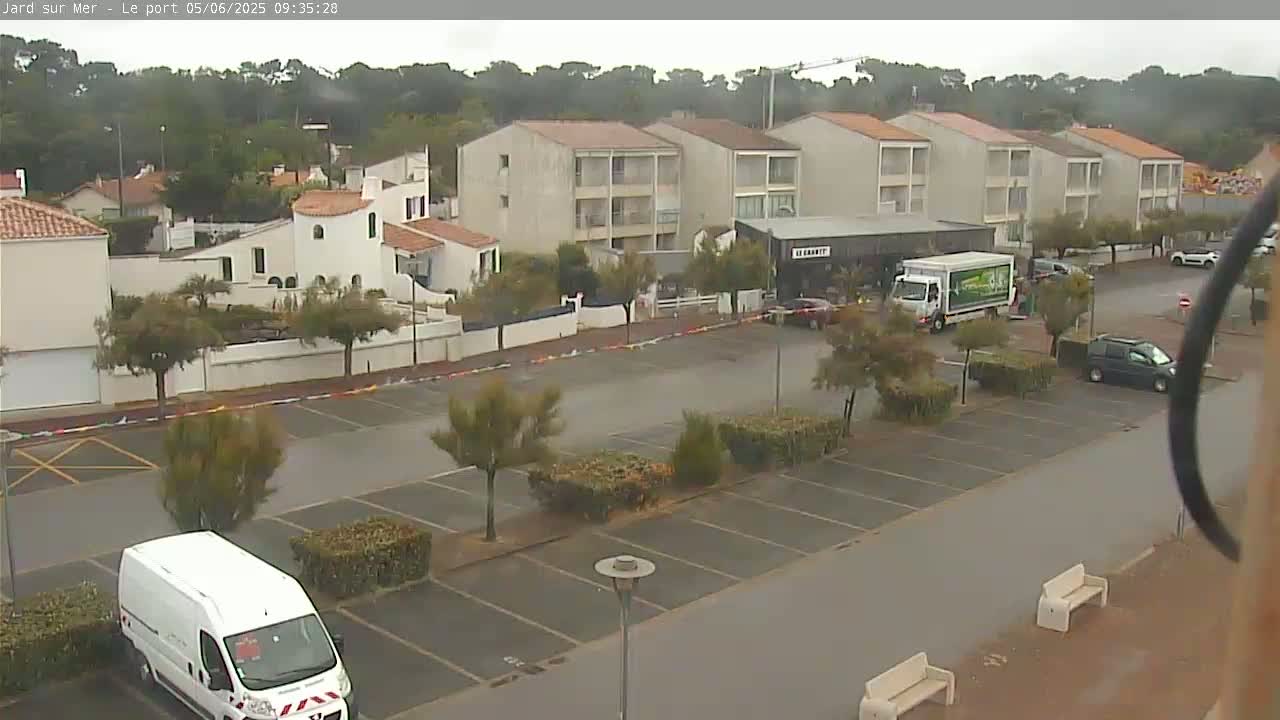 A wet parking lot sits in front of several apartment buildings and small businesses under an overcast sky.