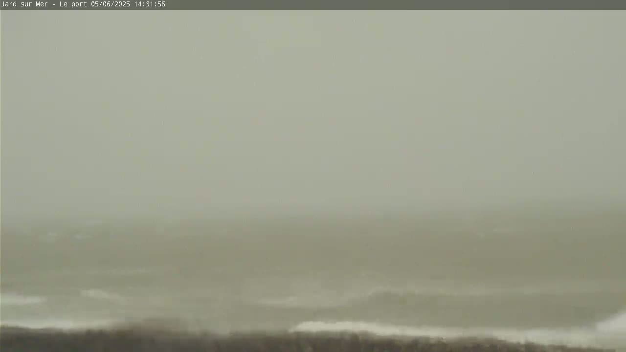 A hazy, overcast day shows a choppy sea with small waves breaking near a shoreline.