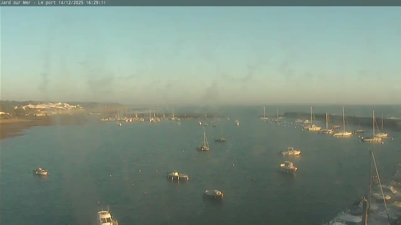 A wide sandy beach, backed by a rocky intertidal zone and the ocean under an overcast sky, is separated by a white barrier from a foreground of rocks and sparse vegetation.