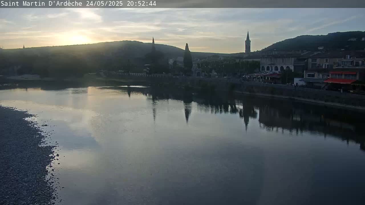 A calm river reflects the setting sun and a small town nestled against hills.
