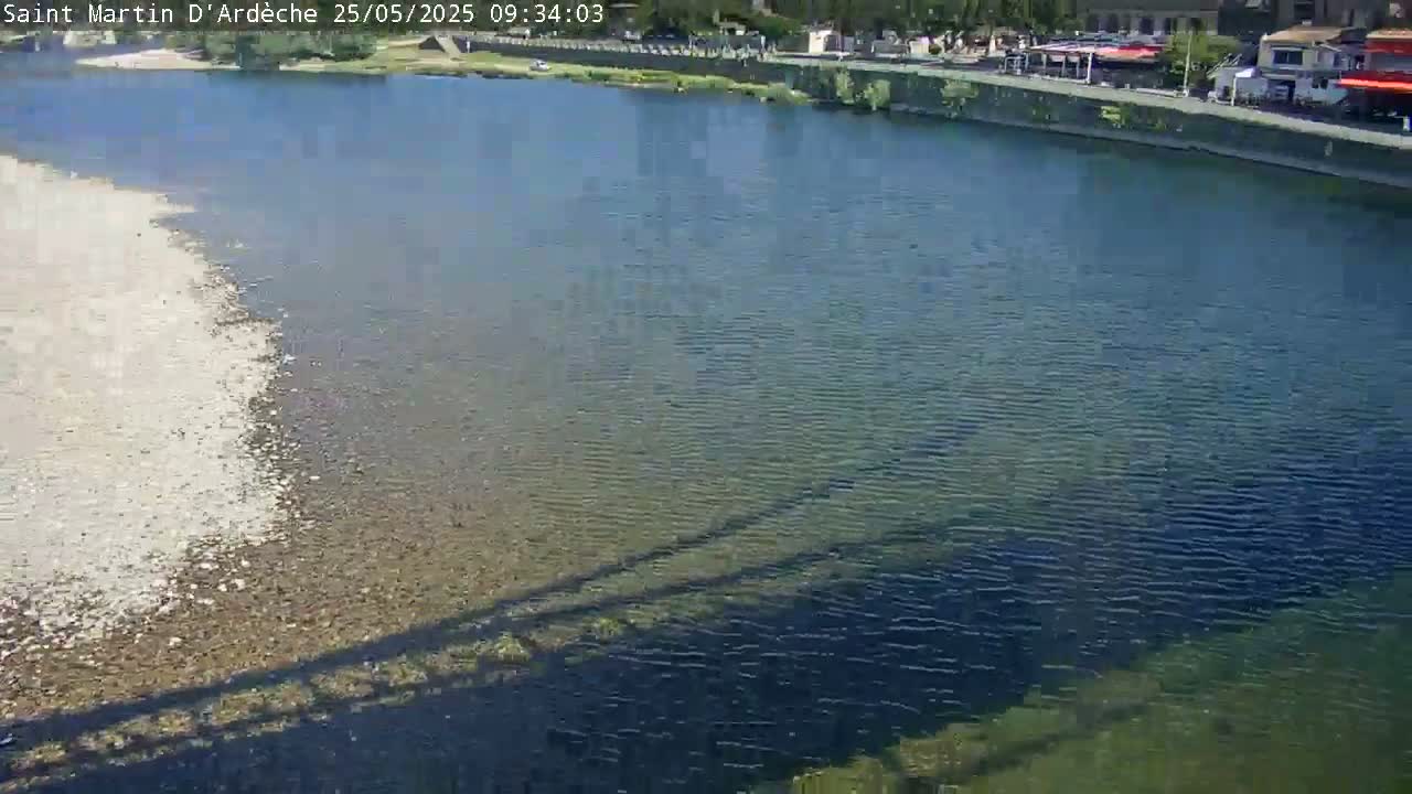 A calm river with a light-colored, shallow section next to a deeper, darker section, seen from a high vantage point on a sunny day.