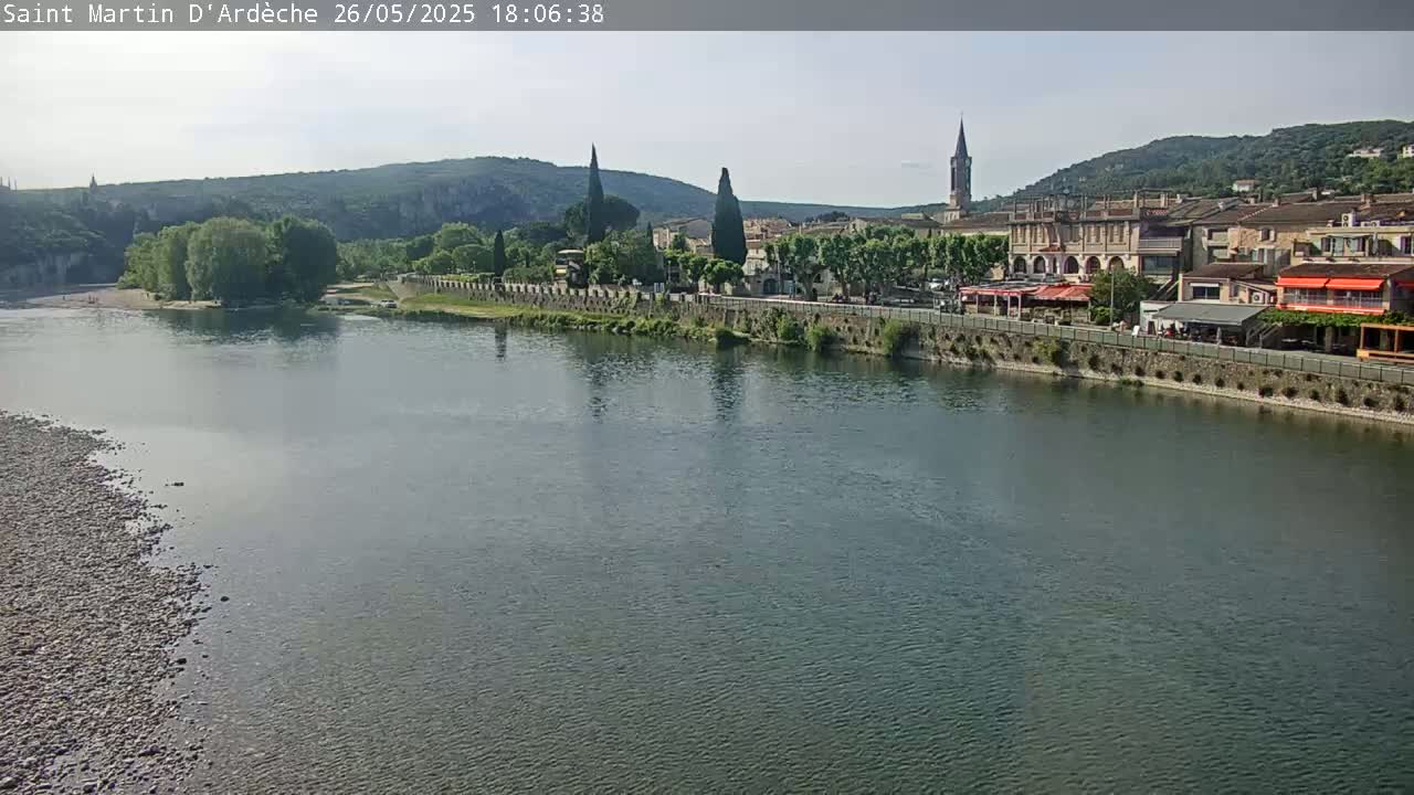 A river flows past a town nestled in a valley under a clear sky.