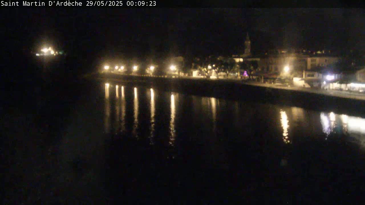 A nighttime view of a calm river reflecting the lights of a town along its edge.