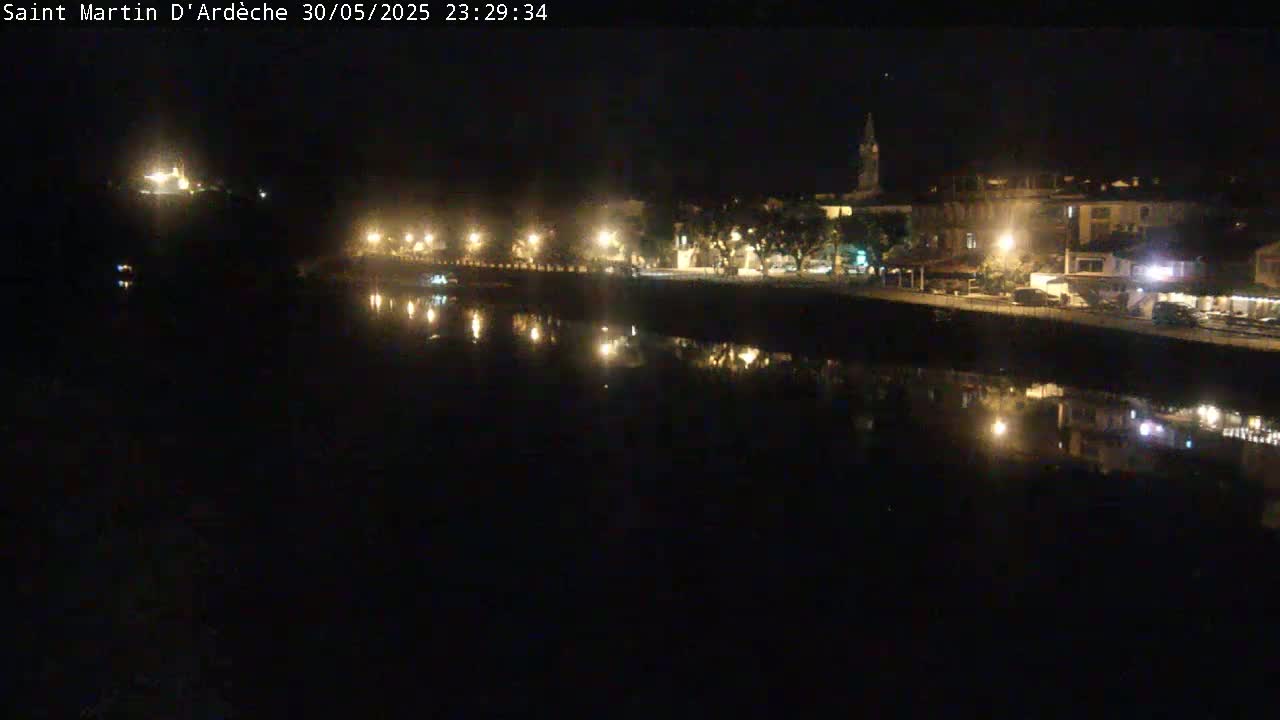 A nighttime view of a town's waterfront, with lights reflecting on a calm body of water.