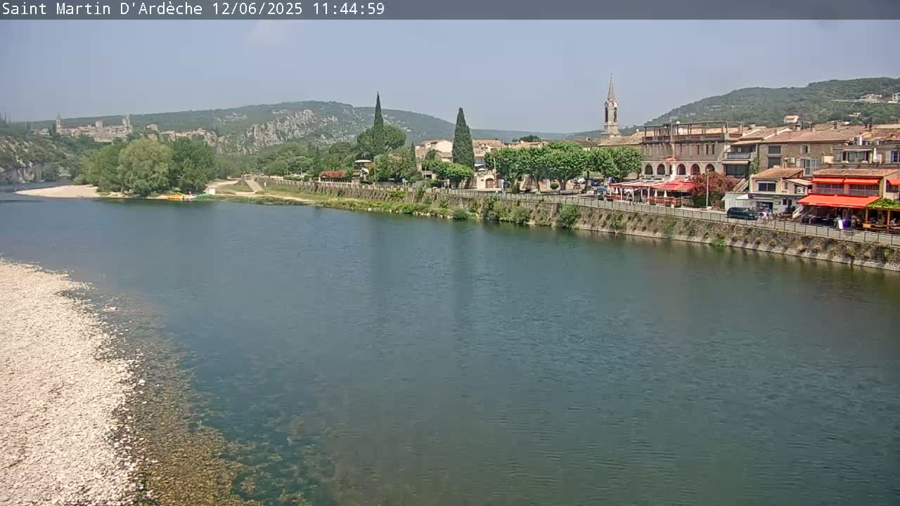 A river flows past a village nestled in a valley under a clear sky.