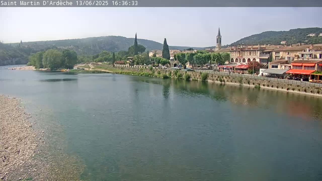 A river flows past a town nestled in a valley under a mostly clear sky.
