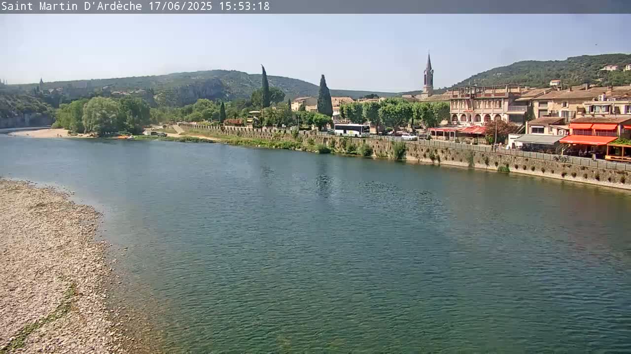 A river flows past a town nestled against hills under a clear sky.