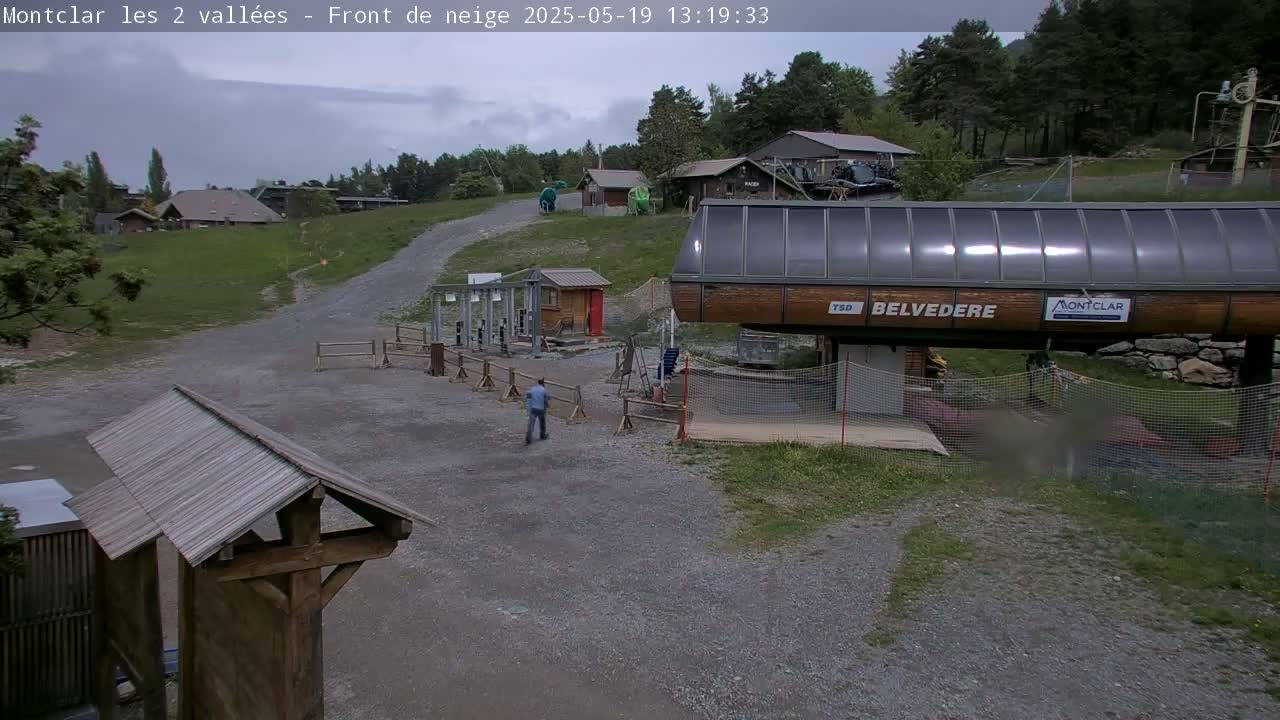 A ski lift station with overcast skies and a person walking nearby.