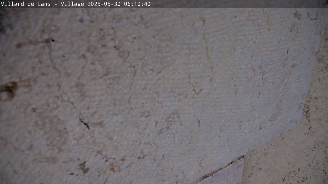 A close-up shows a light-colored, textured wall with numerous thin cracks running through it.