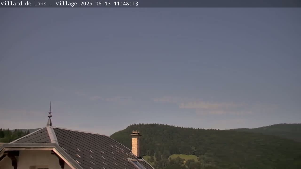 A mostly clear sky overlooks a dark-roofed house and a line of dark green hills.