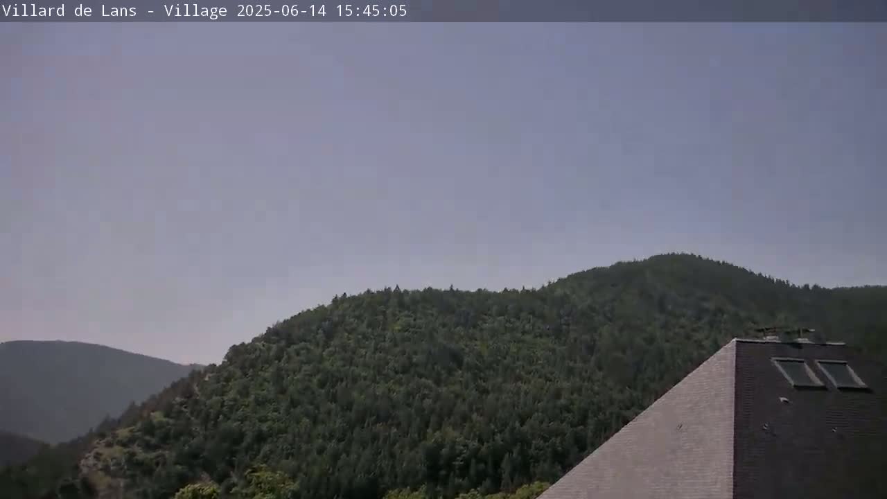 A partly cloudy sky overlooks a lush green mountain range and the corner of a pyramid-shaped building.