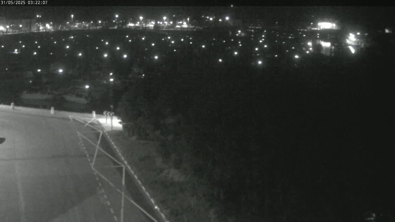 A nighttime, high-angle view shows a road curving to the right with a sparsely lit area beyond it.