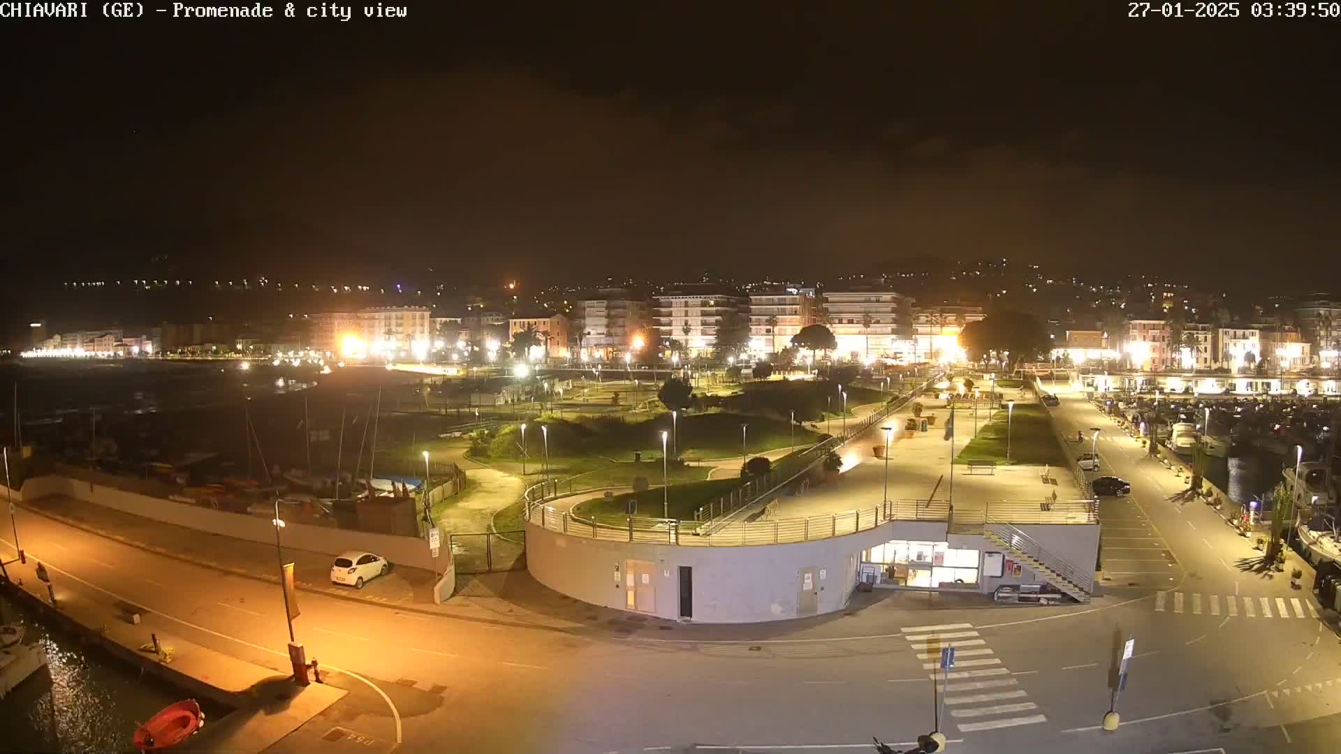 A nighttime aerial view of a city's waterfront promenade and marina, illuminated by artificial lights.