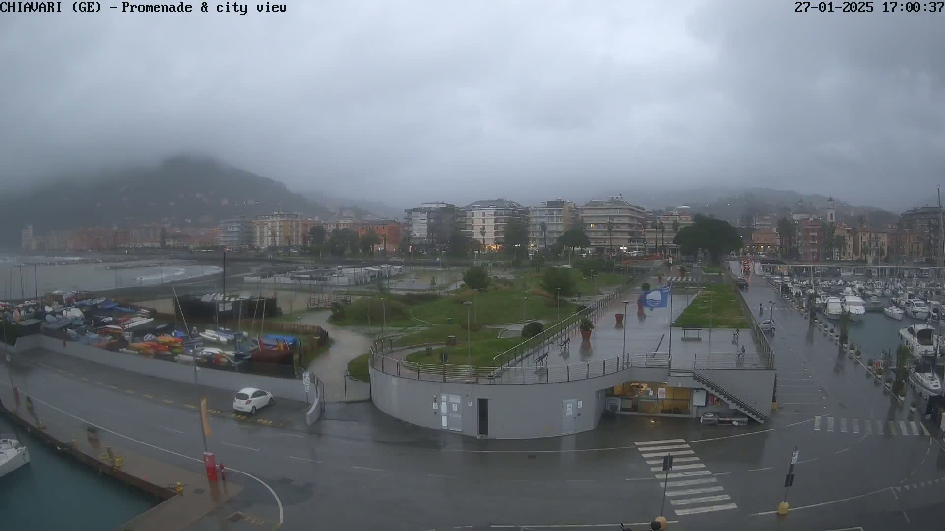 A rain-soaked waterfront promenade and marina are shown, with a city and mountains in the background under an overcast sky.