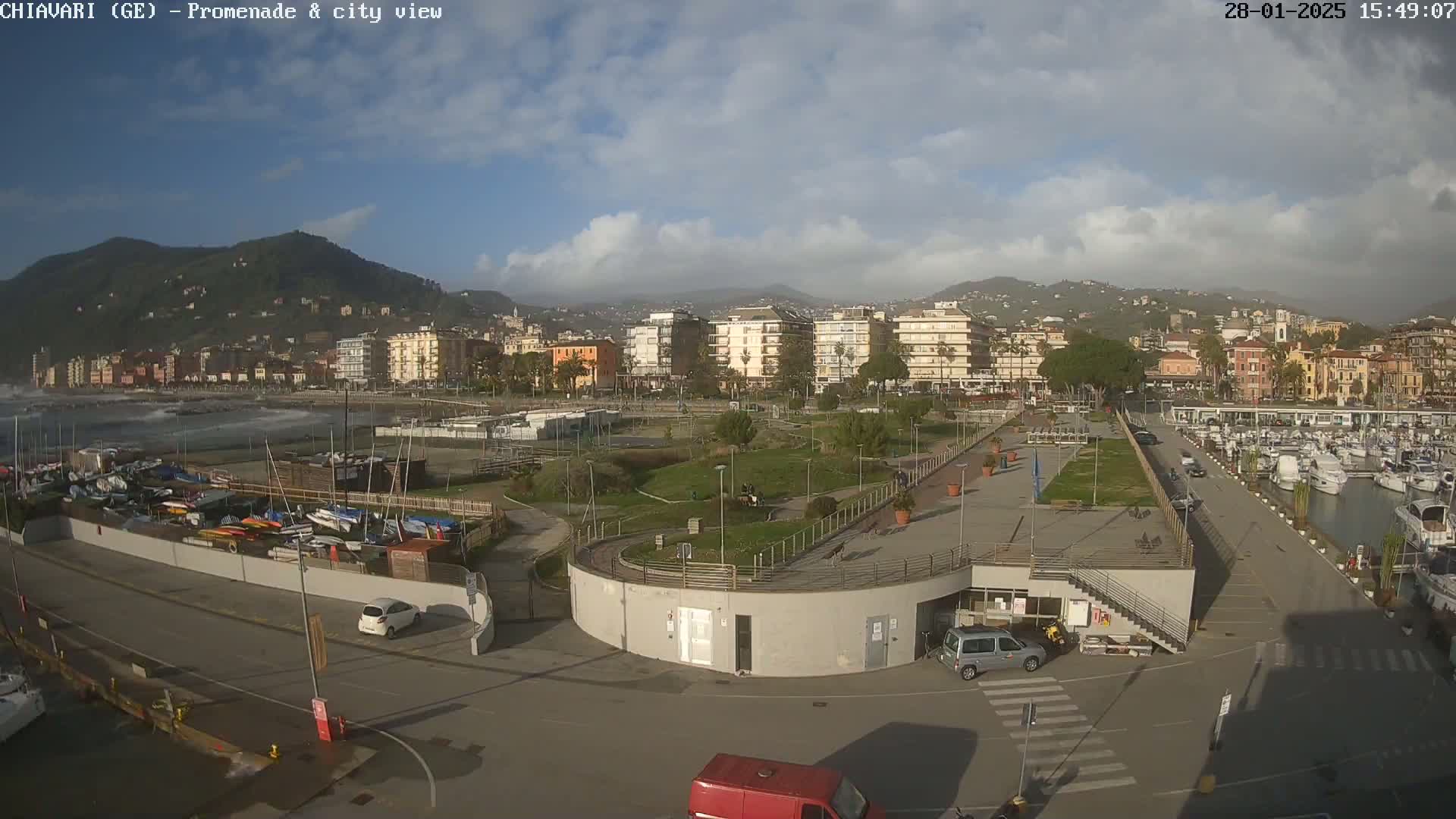 A coastal city with a marina and promenade is seen on a partly cloudy day with choppy water.