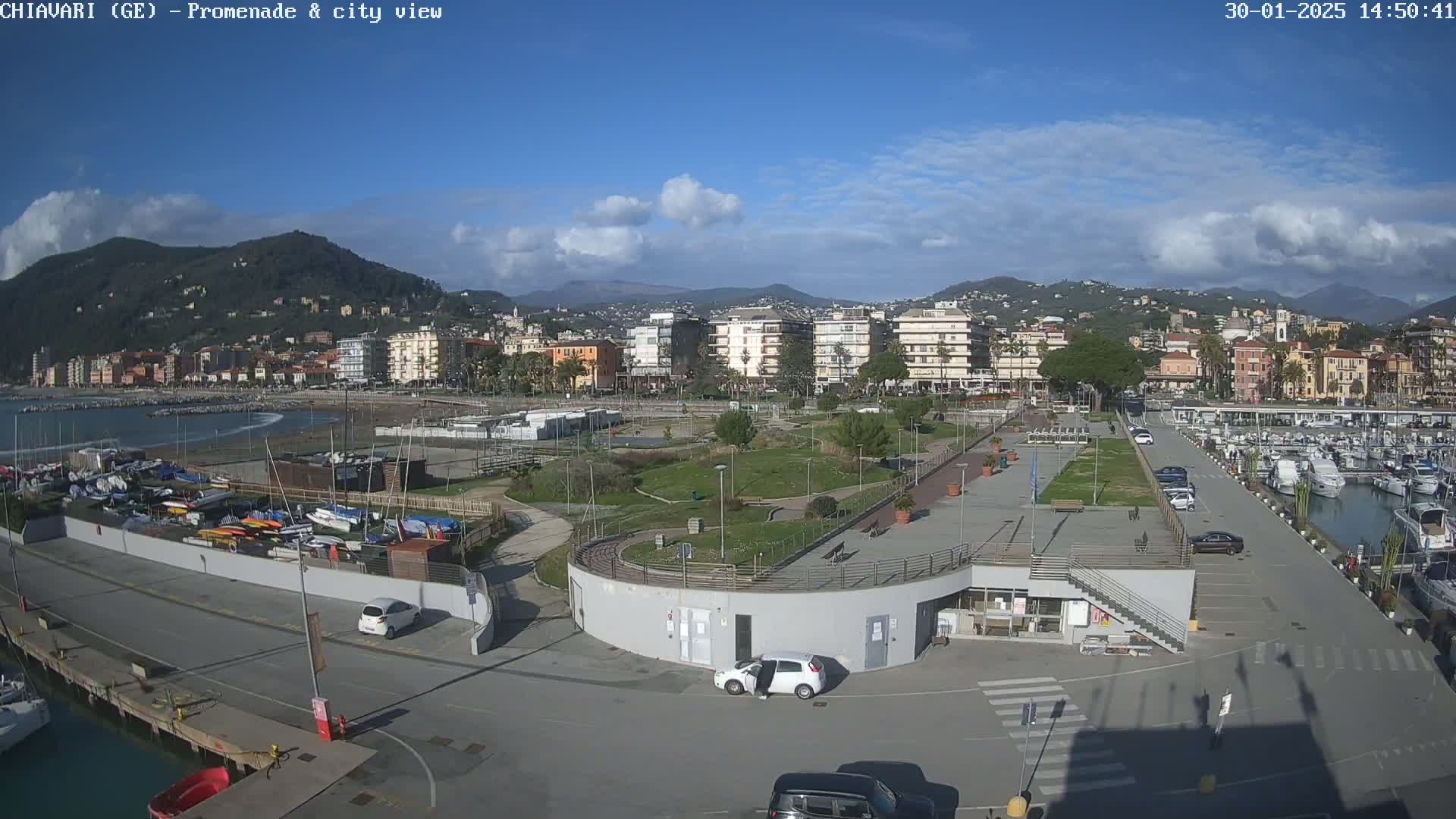 A coastal city with a marina, promenade, and park is shown under a mostly sunny sky with some clouds.