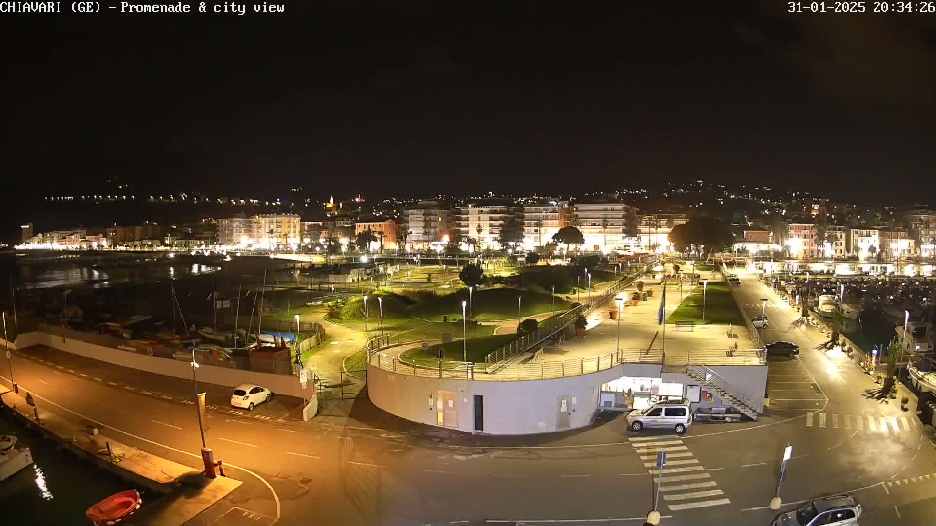 A nighttime aerial view of a harbor and city, with a promenade and park illuminated, under a clear, dark sky.